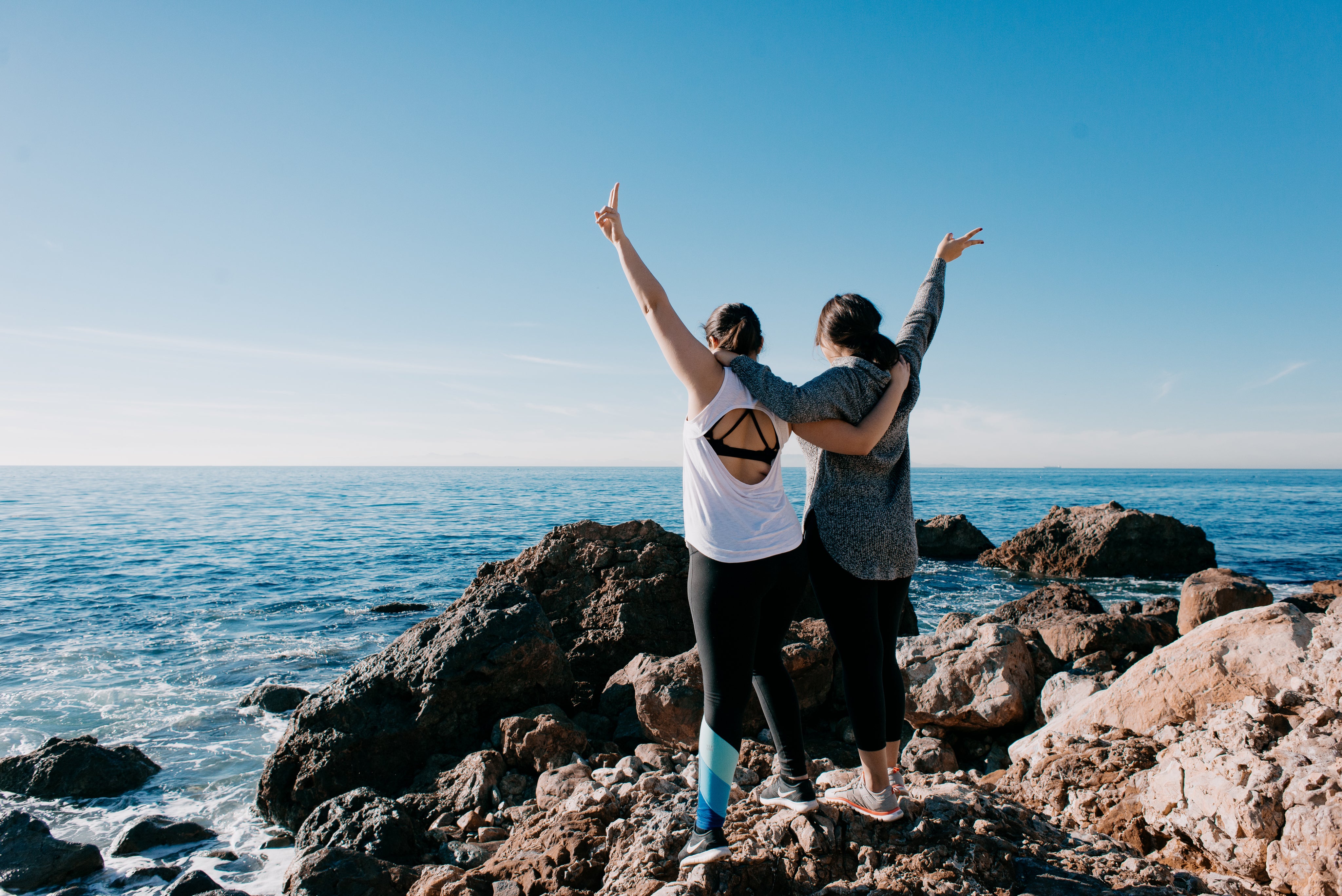 women-arm-in-arm-raise-their-hands-in-peace-sign-on-beach.jpg